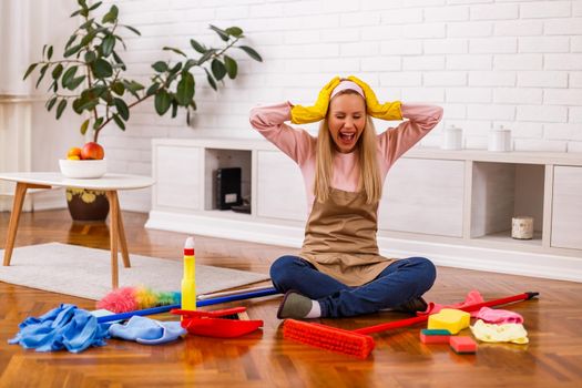 Image of  overworked housewife with cleaning equipment shouting while sitting in the living room.