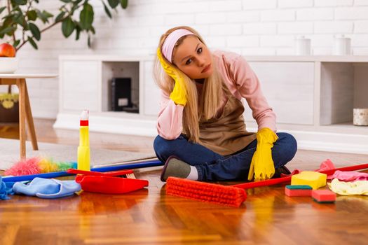 Tired housewife with cleaning equipment sitting in the living room.