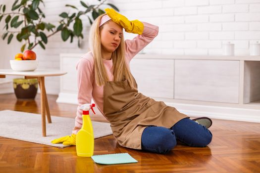 Tired housewife with cleaning equipment sitting in the living room.