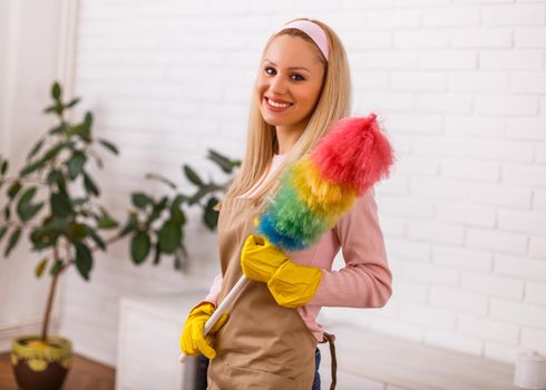 Beautiful housewife enjoys cleaning with duster her home.