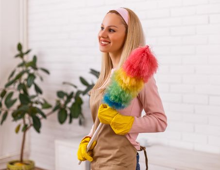 Beautiful housewife enjoys cleaning with duster her home.