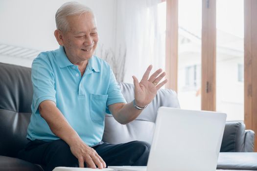 Elderly man making video call and waving at screen, chatting with children, communication with friend distantly, older generation modern tech easy comfortable usage concept.