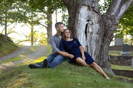  beautiful brunette leans and relaxes against her handsome husband outside at a park 