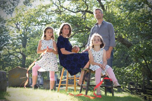 a solemn looking parents and daughters in a cemetery on a sunny day, looking to the heavens