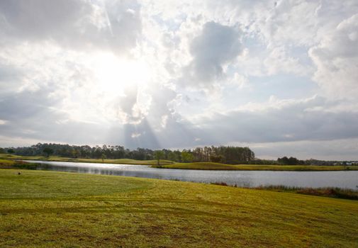 sun peeking through the clouds at early morning on a florida golf course beside a pond 