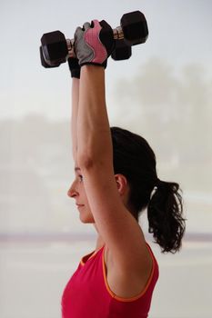 young woman lifting weights above her head to strengthen shoulders and arms