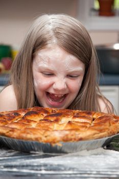 A little girl covered in flour after baking or food fight laughing and looking over an apple pie.