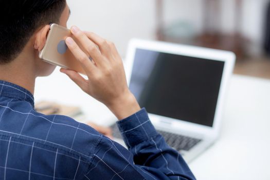 Young asian man talking phone and work from home with laptop computer, freelance using notebook to internet online and speak on smartphone, domestic life, business and communication concept.