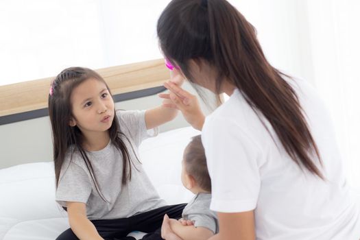 Young asian mother and daughter sitting playing with little baby girl on the bed together, mom and children relax, family of emotion and expression with happiness, parent and newborn, indoor.