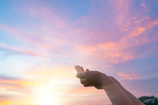 Woman hands place together like praying in front of nature green bokeh and blue sky background.