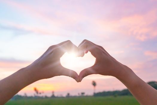 Woman hand do heart shape on nature blue sky background.