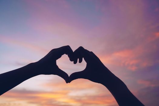 Woman hand do heart shape on nature blue sky background.