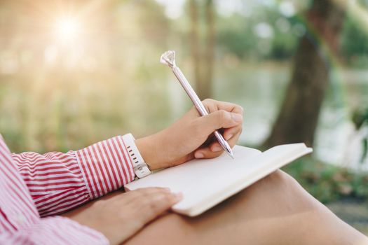 Woman hand writing down in small white memo notebook for take a note not to forget or to do list plan for future in public park.