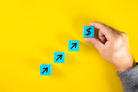 Hand completing conceptual set of business growth on wooden cubes with black arrows and dollar. Yellow background