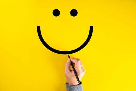Male hand drawing a smiling happy face sketch on yellow background. Client satisfaction, service or product evaluation concept.