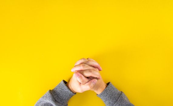 The hands of the man who was clinging to the prayer on the book on the yellow background.Top view