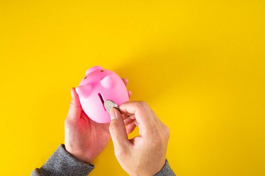 Hand puts a coin into the piggy bank coin on a yellow background.