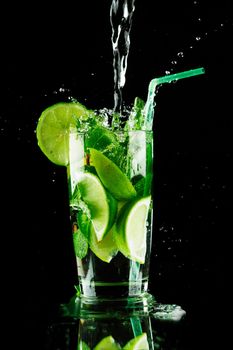 Pouring fresh mojito cocktail in glass notion ice splashing isolated on black background