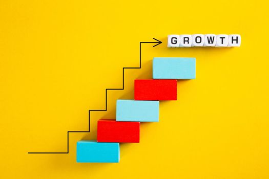 An upward pointing arrow on top of growing graph made of wooden blocks over yellow background