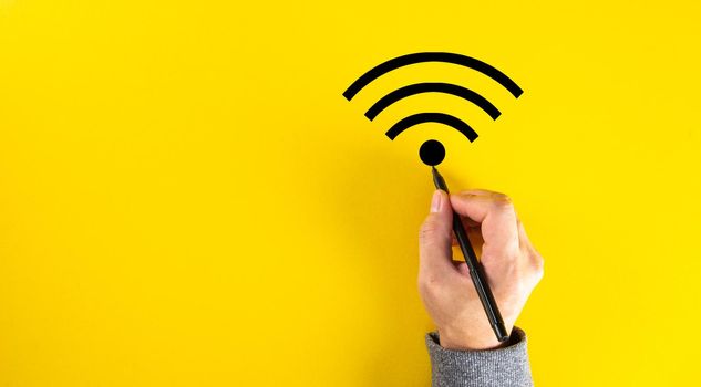 Male hand drawing a wifi signal on yellow color background with copy space.