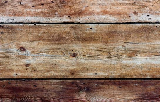 Boards of aged wood arranged horizontally. The wood is weathered, heavily textured and coloured yellow, gold and brown.