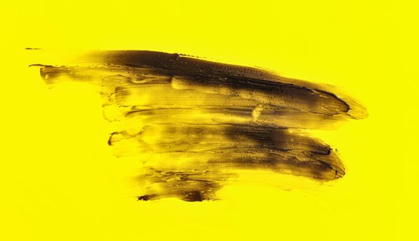 Black smears charcoal toothpaste over yellow board, abstract background.