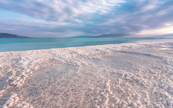 Morning sun shines on salt crystals formations, clear cyan green calm water near, typical landscape at Ein Bokek beach, Israel.