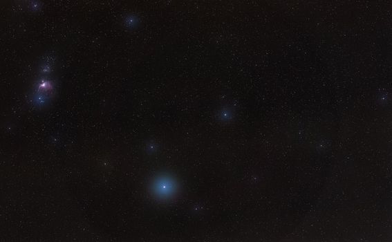 Winter night sky with purple Orion nebula, bright blue Rigel star - diffused through some clouds - in bottom lower part, long exposure photo.