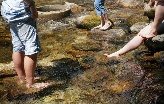 Group of people walking in forest river or cooling their bare feet, detail on legs only.