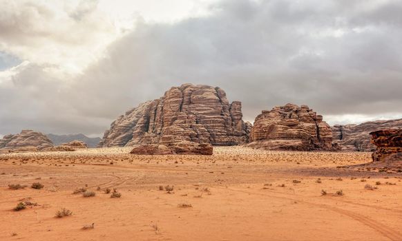 Rocky massifs on red orange sand desert, overcast sky in background - typical scenery in Wadi Rum, Jordan.