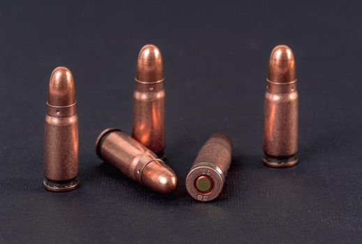 Five bronze pistol bullets on black board, closeup detail.