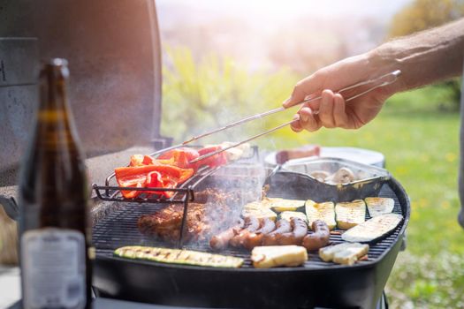 Close up of sausages, steak, cheese and vegetables on gas grill. Summer time, outdoors.