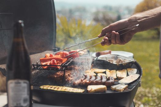 Close up of sausages, steak, cheese and vegetables on gas grill. Summer time, outdoors.