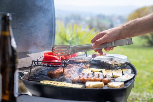 Close up of sausages, steak, cheese and vegetables on gas grill. Summer time, outdoors.