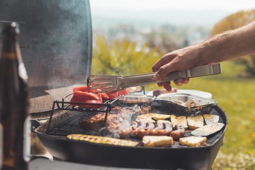 Close up of sausages, steak, cheese and vegetables on gas grill. Summer time, outdoors.