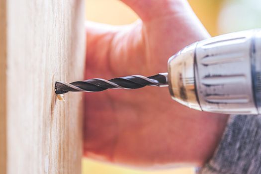 Do it yourself home handyman is using a drill for drilling wood