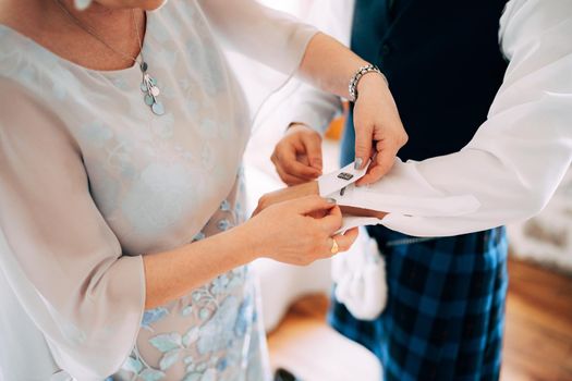 Preparing for a scottish wedding. Woman fastening cufflinks on a shirt of a man in a kilt. High quality photo