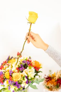 Woman's hand placing yellow rose to flower bouquet