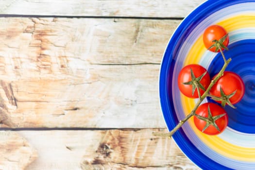 Cherry tomatoes on colorful striped plate and brown wooden background