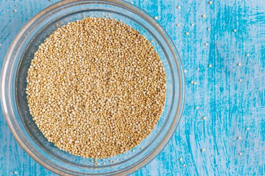 Raw quinoa grains inside transparent bowl, on blue table
