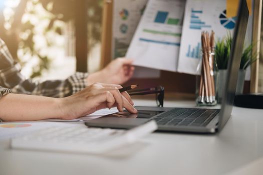 Close up of businessman or accountant hand holding pen working on laptop for business data, accountancy document and laptop computer at office, business concept..