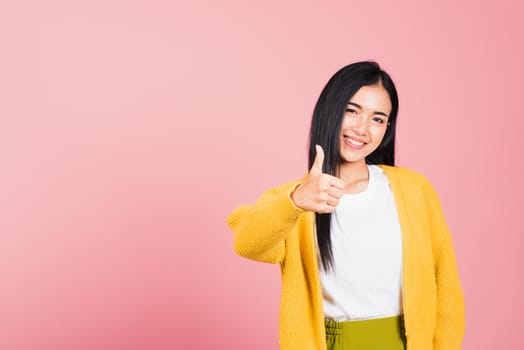 Portrait Asian beautiful young woman smile she standing made finger thumbs up, Ok sign to agree studio shot isolated on pink background, Thai female successful like finger gesture with copy space