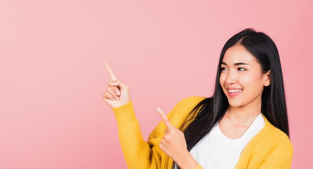 Asian happy portrait beautiful cute young woman standing makes gesture two fingers point upwards above presenting product something, studio shot isolated on pink background with copy space