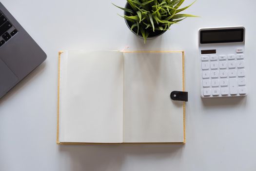 Modern white office desk table with calculator and laptop computer. Blank notebook page for input the text in the middle. Top view, flat lay