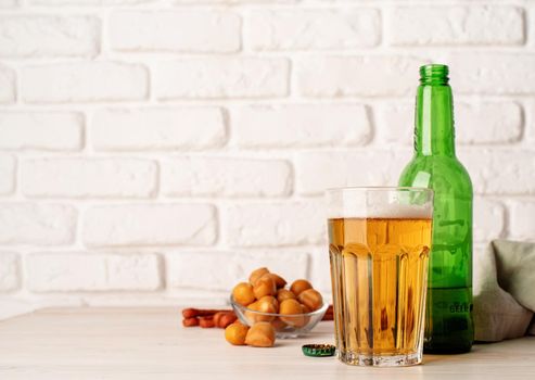 Full glass of beer, bottle and snacks, white brick wall background on white brick wall background. Copy space, front view