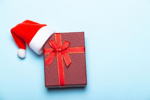 Red gift on a blue background . A gift with a Santa hat. Christmas and new year. A gift for the holiday. Red gift wrap.