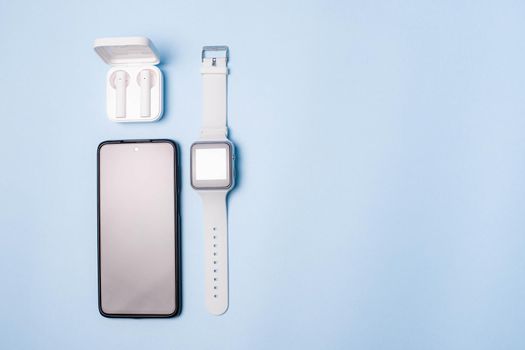 The layout of the watch and the phone on a blue background. Appliances and electronics. Modern gadgets. Phone headphones watch. Business. Student. Wireless headphone. Watch with pedometer. Copy space