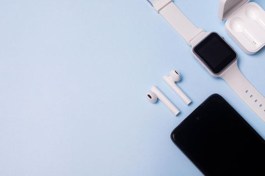 The layout of the watch and the phone on a blue background. Appliances and electronics. Modern gadgets. Phone headphones watch. Business. Student. Wireless headphone. Watch with pedometer. Copy space