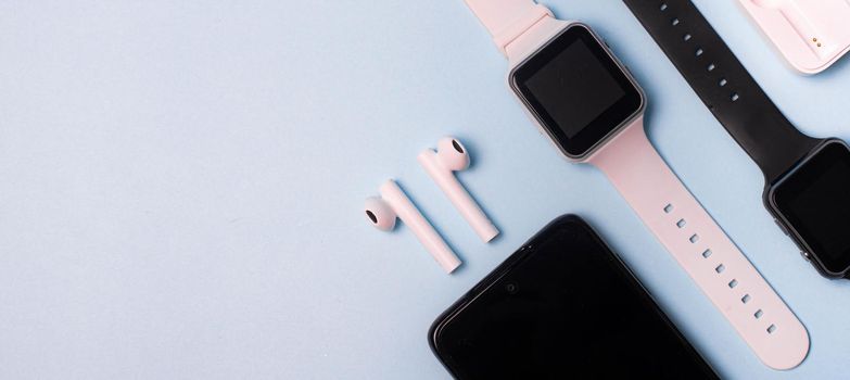 The layout of the watch and the phone on a blue background. Appliances and electronics. Modern gadgets. Phone headphones watch. Business. Student. Wireless headphone. Watch with pedometer. Copy space