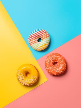 Creative layout made from delicious glazed donuts. Vertical flat lay - donuts or doughnuts on colorful background with copy space. Blue, yellow and pink geometric background.